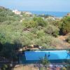 Vista su una piscina nel verde, circondata da alberi. Sullo sfondo, mare e colline.