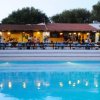Piscina illuminata di fronte a un edificio con veranda e ospiti seduti.