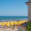 Una spiaggia sabbiosa con lettini e ombrelloni davanti a un grande edificio bianco e colline verdi.