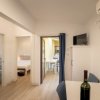 Un interno moderno con sala, tavolo, bottiglia di vino, camera e bagno visibili con parquet chiaro.